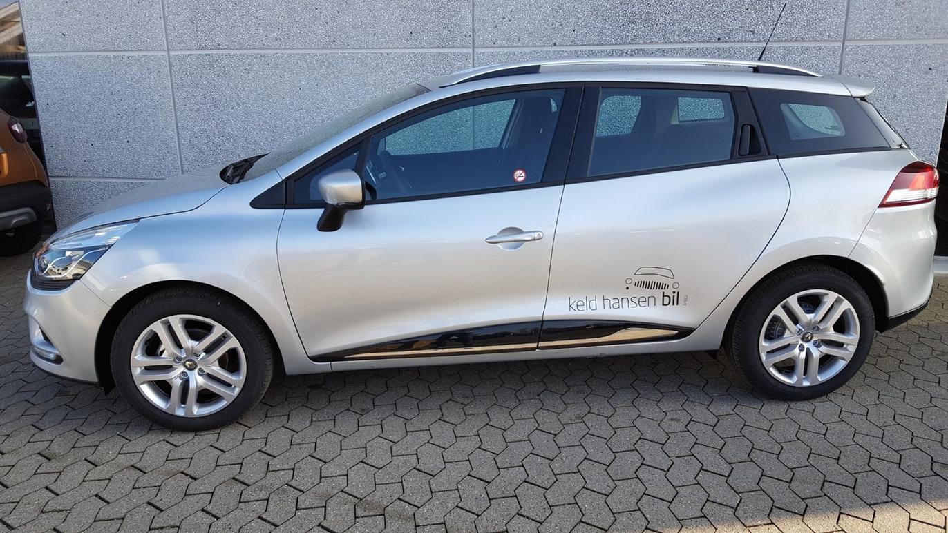 En sølvfarvet bil parkeret på en flisebelagt overflade, set fra siden med en moderne design.