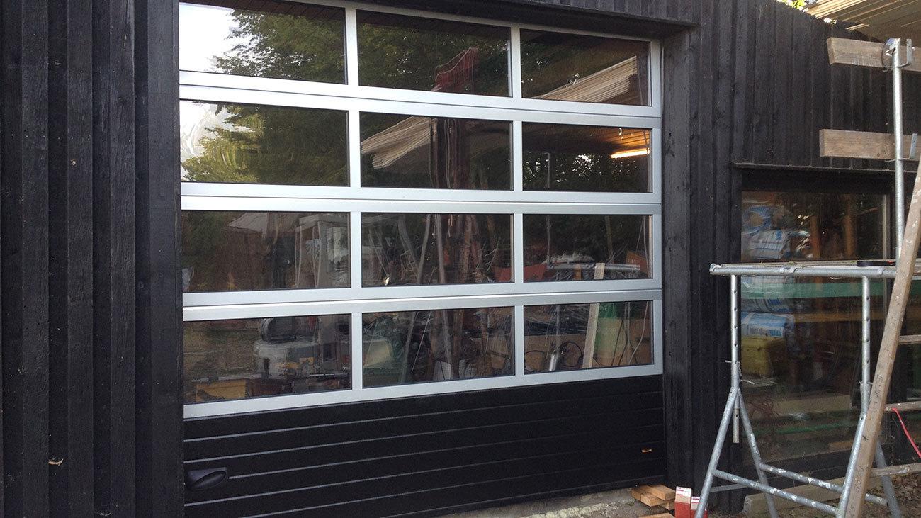 En moderne garageport med glasruder og sort træbeklædning på en bygning.