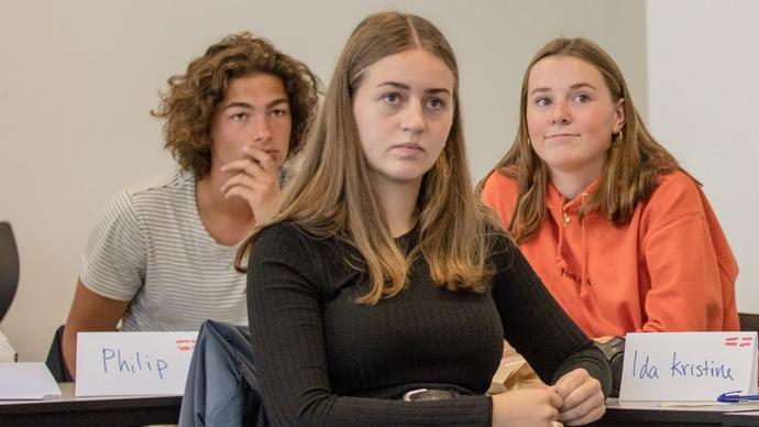 Tre unge mennesker sidder i et klasseværelse, fokuseret på en præsentation.