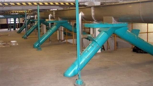 Rørledninger og ventilationssystem i en industriel bygning med grønne rør og metalstøtter.