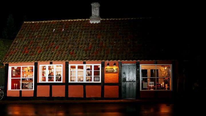 En hyggelig, oplyst bygning med røde vægge og grønne vinduer, set om natten.