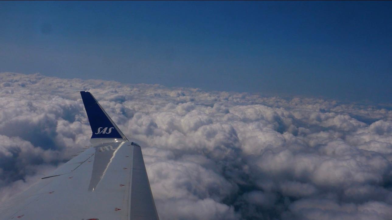 Udsigt fra et fly med SAS vinger over en skyfyldt himmel.