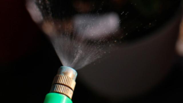 Sprinkler med grøn slange, der sprøjter vand i fine dråber over en plantepotte.