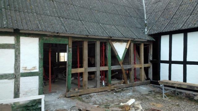 Renovering af et gammelt hus med synlige trærammer og en stråtag. Byggeplads med værktøj og materialer.