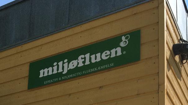 Skilt med teksten "miljøfluen" på en gul trævæg, beliggende i et lyst miljø.