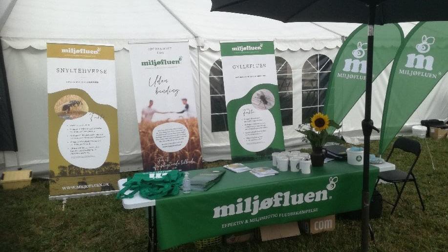 Billede af en messestand med bannere og en grøn dug, der promoverer miljøfluen og bæredygtighed.
