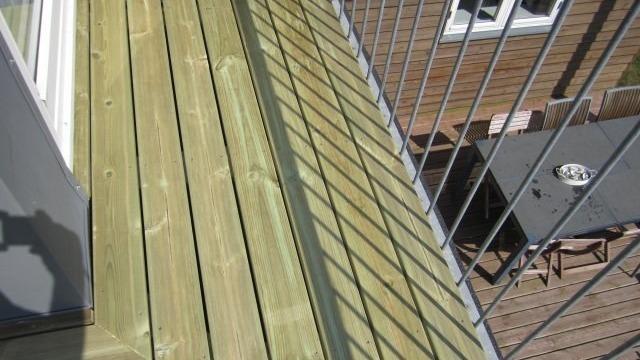Balkon med trædæk og metalgelænder, der kaster skygger på overfladen.