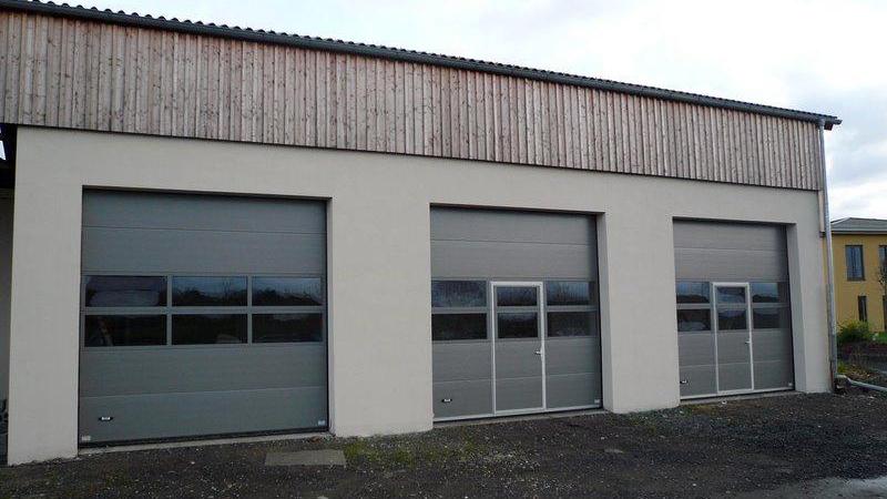 En bygning med tre grå garageporte og en træbeklædning på taget.