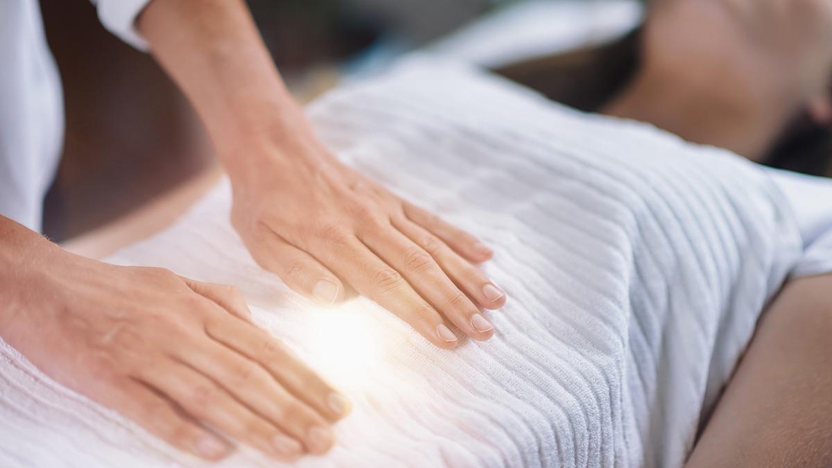 Hænder udfører healing på en person, der ligger på en behandlingsbriks med hvidt lagen.