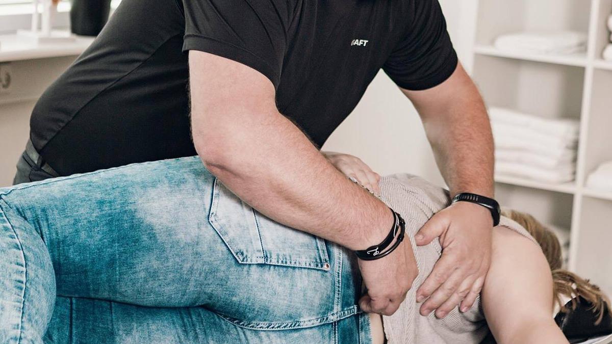 En behandler udfører en rygbehandling på en patient, der ligger på en behandlingsbænk.