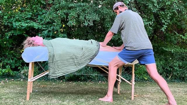 En person får massage på en massagebriks i en have, mens en anden person giver massage.