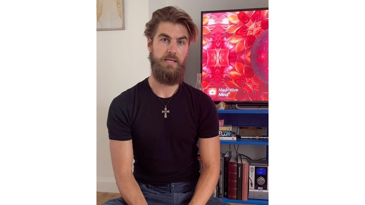 En mand med skæg iført en sort t-shirt sidder foran en tv-skærm med farverige mønstre.