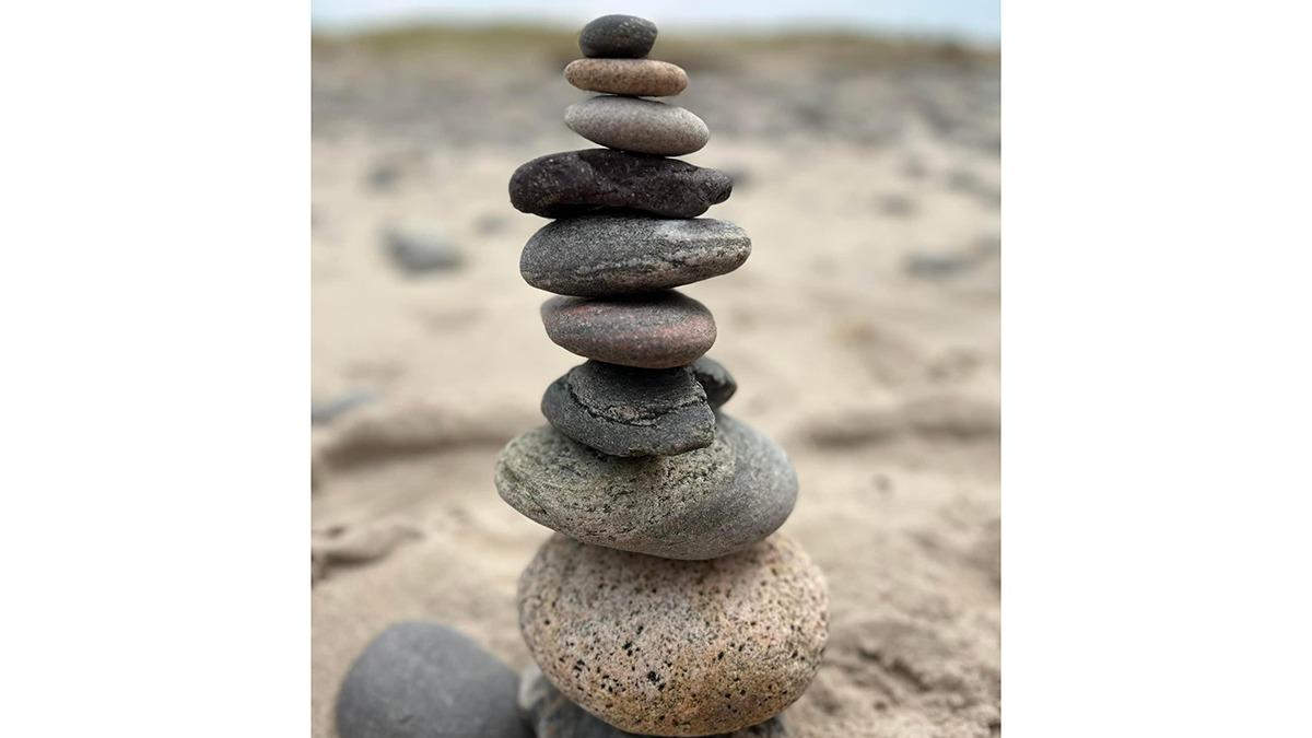 En stak af glatte sten i forskellige farver på en sandstrand.