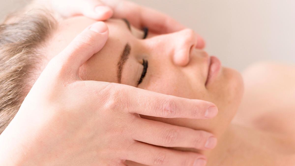 En kvinde får en afslappende ansigtsmassage med hænderne fra en behandler.