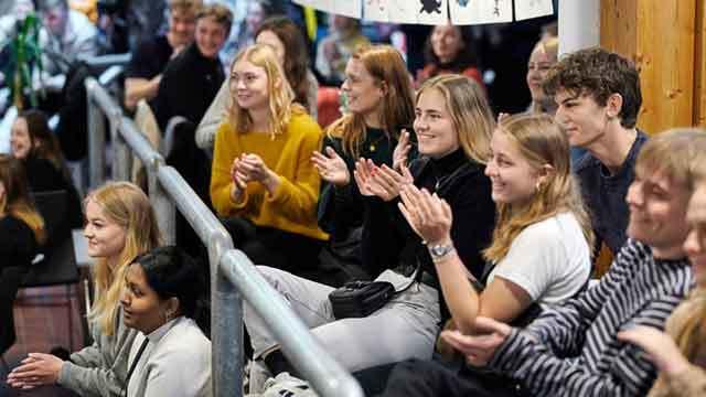 En gruppe unge mennesker sidder og klapper, mens de ser en præsentation i et auditorium.