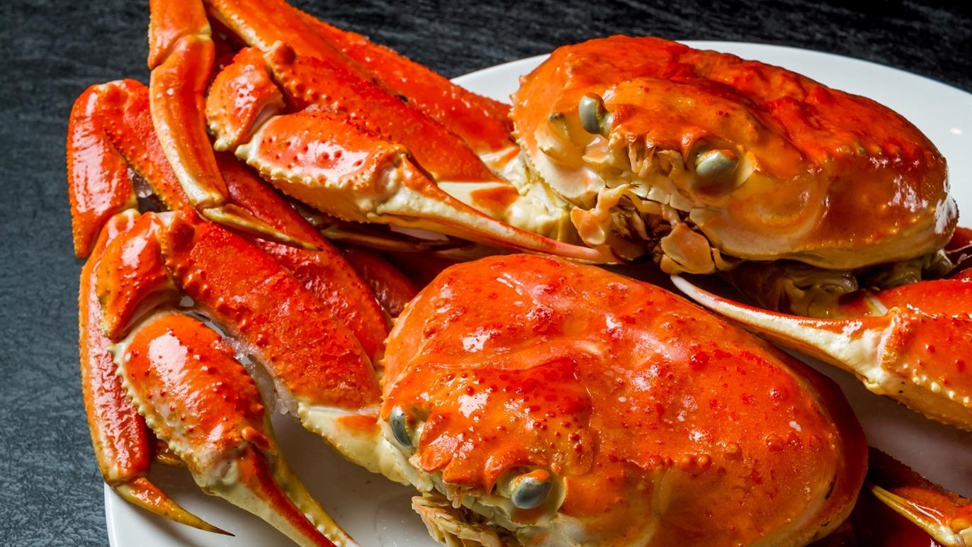 En tallerken med kogte krabber, der har en lys orange farve og er placeret på en sort overflade.
