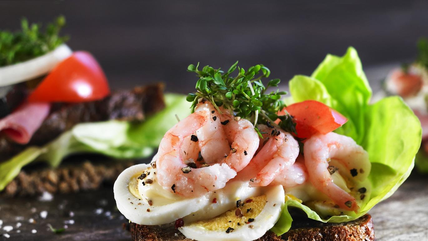 Lækre smørrebrød med rejer, æg, salat og tomater på rugbrød, prydet med friske krydderurter.