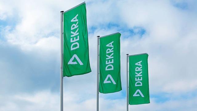 Tre grønne flag med teksten "DEKRA" svajer i vinden under en skyet himmel.