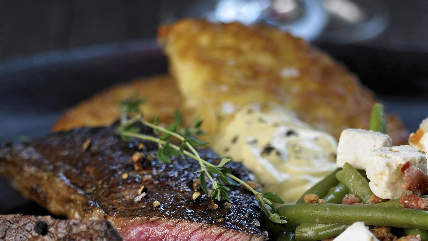Saftig bøf med krydderurter, sprød kartoffelrösti og grøntsager på en sort tallerken.