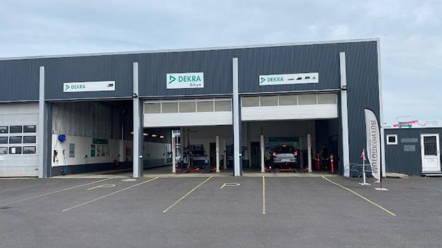 Bilværksted med tre porte, logoer og parkeringspladser foran bygningen.