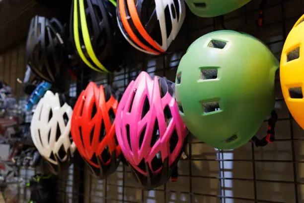 Farverige cykelhjelme hænger på en væg, herunder grøn, pink, rød og hvid, klar til salg.