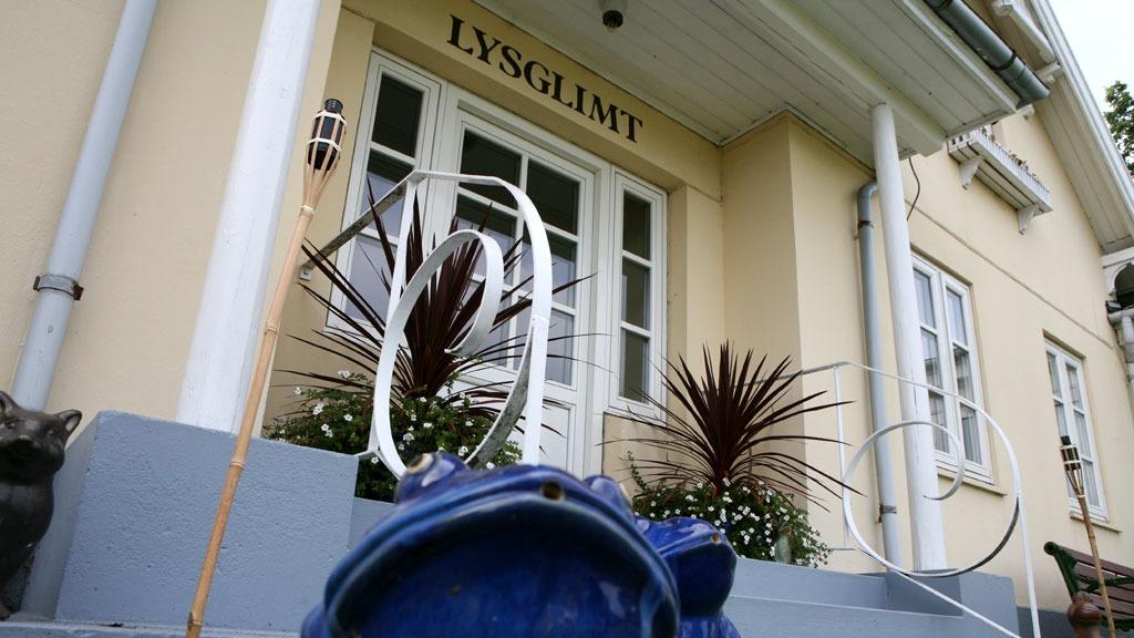 Blå skulptur foran bygning med teksten "LYSGLIMT" og planter ved indgangen.