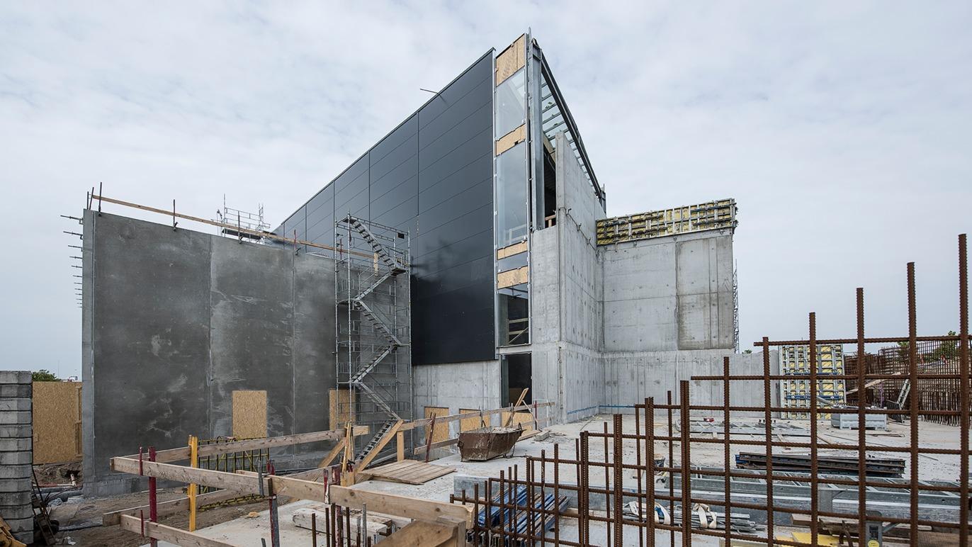 Byggeri af moderne bygning med betonvægge og metalfacade under konstruktion. Stålrammer og stilladser er synlige.