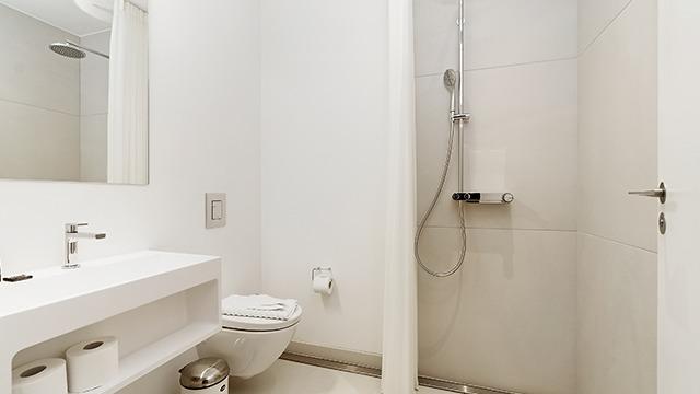 Moderne badeværelse med bruser, toilet og håndvask i minimalistisk design med hvide vægge.