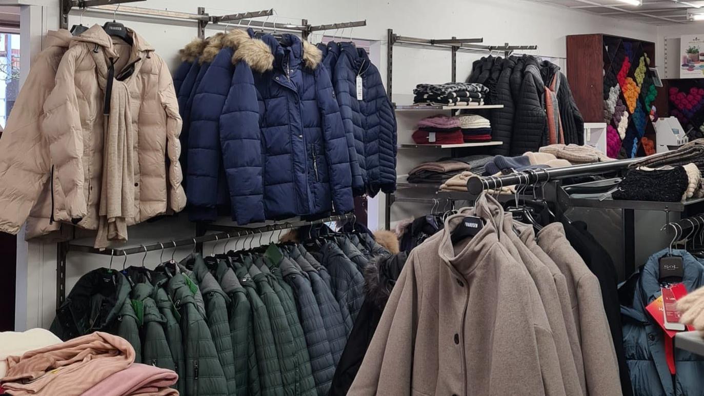 Butik med forskellige vinterjakker hængende på stativer, herunder dunjakker i forskellige farver og stilarter.