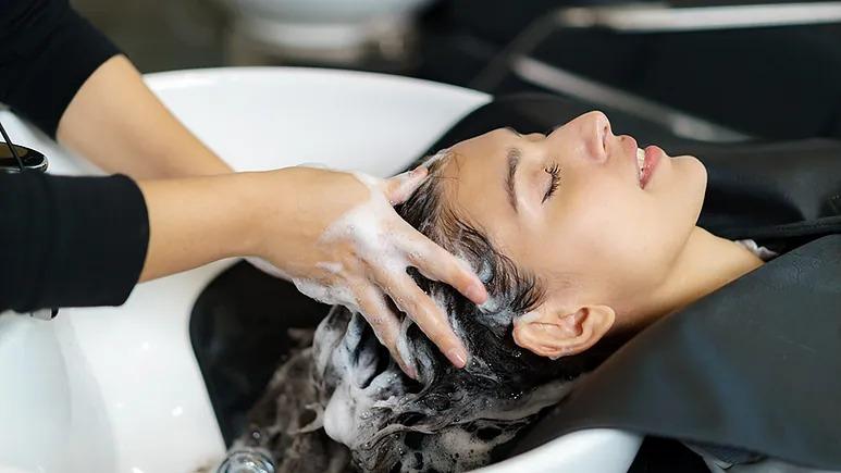 En kvinde får vasket sit hår i en frisørsalon, mens en frisør masserer hendes hoved med shampoo.