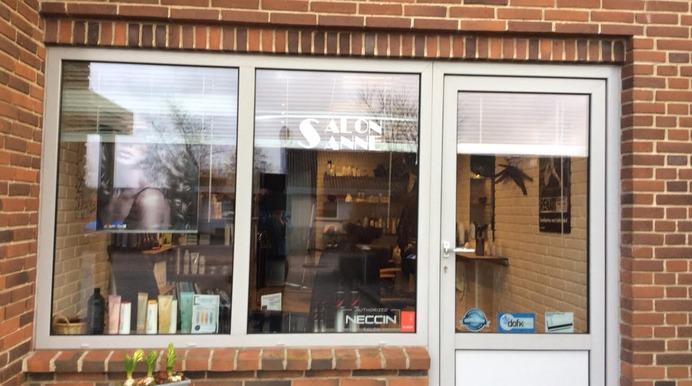 Frontal udsigt af en frisørsalon med store vinduer og en indgangsdør, omgivet af mursten.