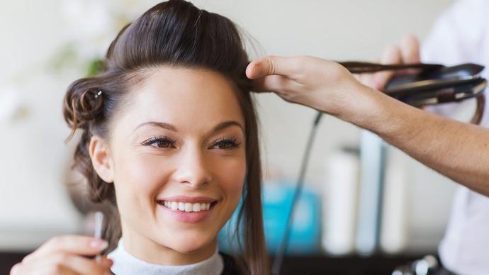 En kvinde får lavet frisørbehandling med glattejern, mens hun smiler i en salon.