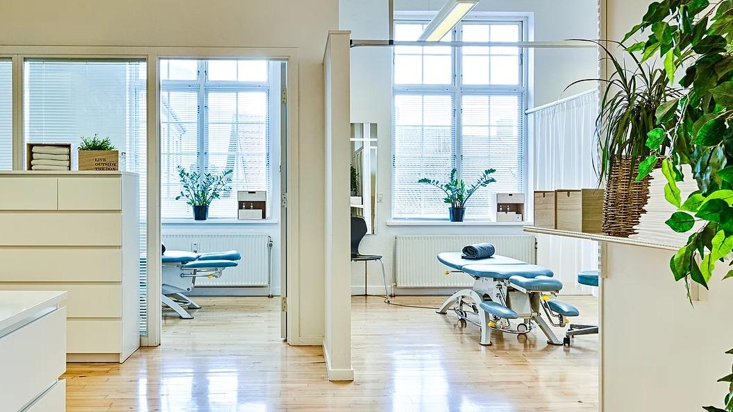 Lyst og moderne tandlægeklinik med behandlingsstole og planter i vinduerne.
