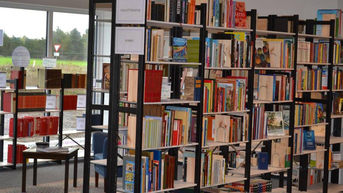 Billede af en moderne bibliotek med reoler fyldt med bøger og en stol i forgrunden.