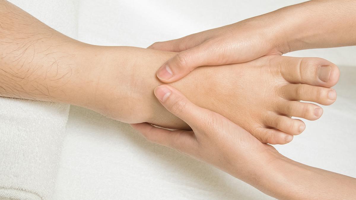 Håndmassage af en fod med fokus på anklen, der giver afslapning og velvære.