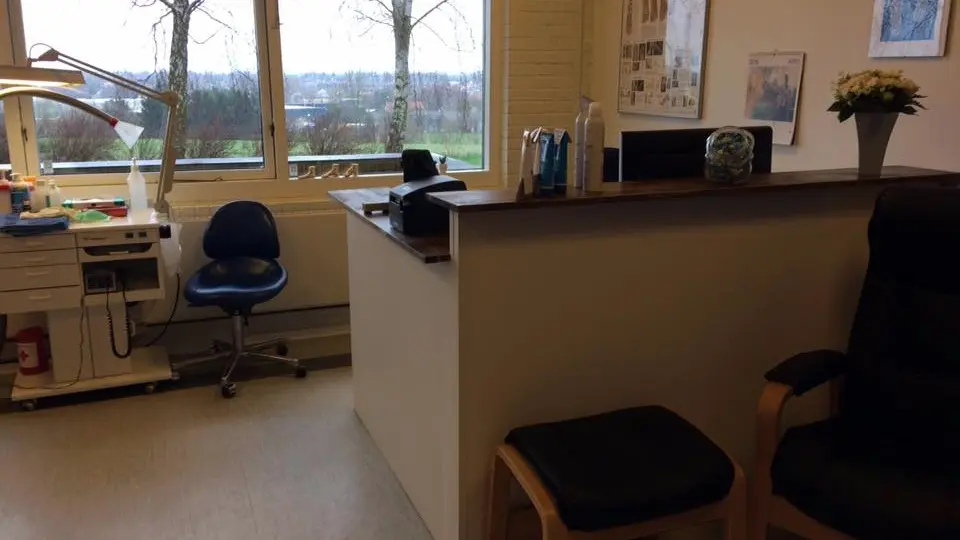 Et kontor med en skrivebordsplads, en stol, og vinduer der viser en grøn udsigt.