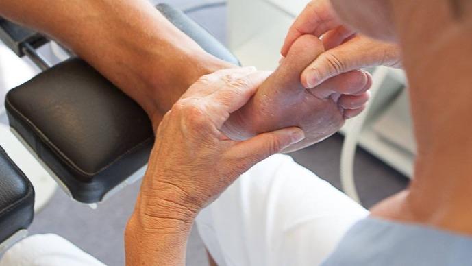 En person får behandling af en fod med fokus på massage af anklen og håndens greb.