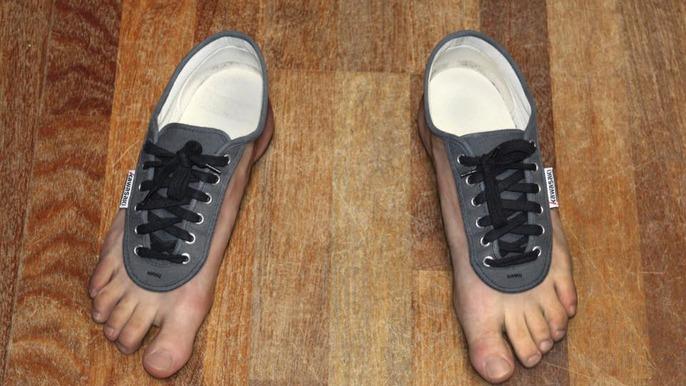To fødder iført grå sneakers med sorte snørebånd på et trægulv.