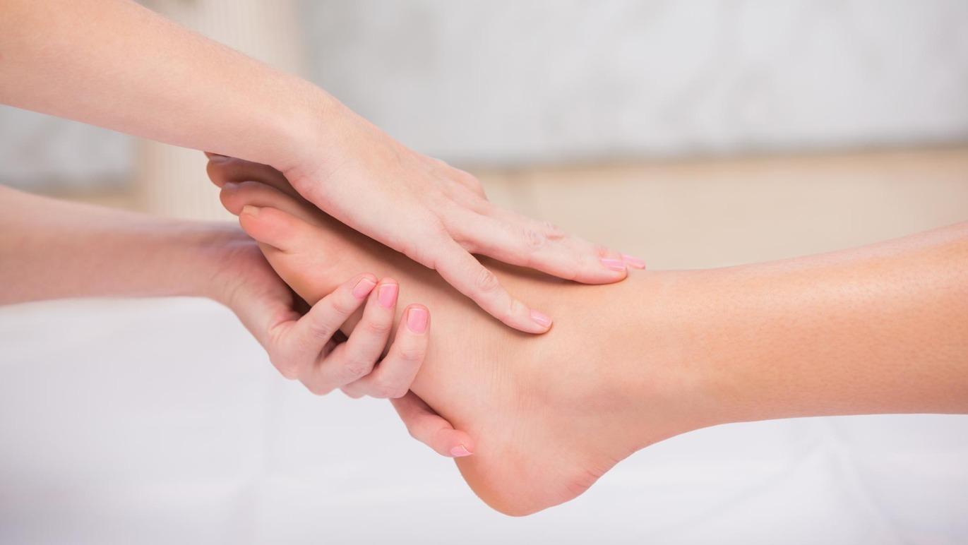 En person får en afslappende fodmassage med hænderne, der trykker blidt på foden.
