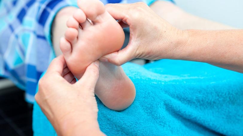 En person får fodmassage, hvor hænderne trykker på foden, mens den ligger på en blå håndklæde.