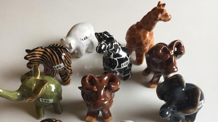 Samling af små porcelænsdyr, herunder elefanter, giraffer og zebraer, arrangeret på en hvid overflade.