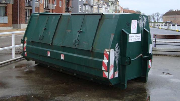 Affaldscontainer i grøn farve placeret på en fortov ved bygninger.