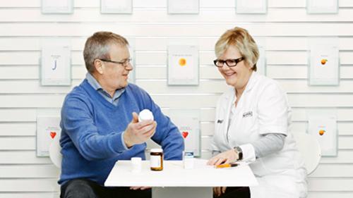 En mand og en kvinde i hvidt arbejdstøj sidder ved et bord og diskuterer medicin.