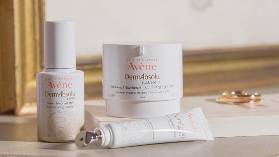 Avene Dermabody hudplejeprodukter i en elegant indstilling med en ramme og smykker i baggrunden.