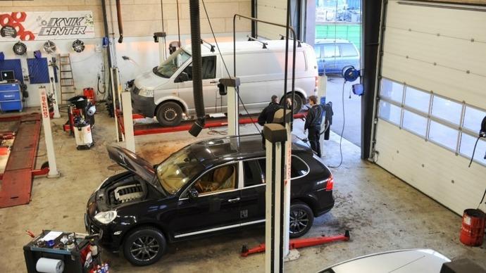 Billede af et bilværksted med flere biler på lifte og mekanikere, der arbejder på reparationer.