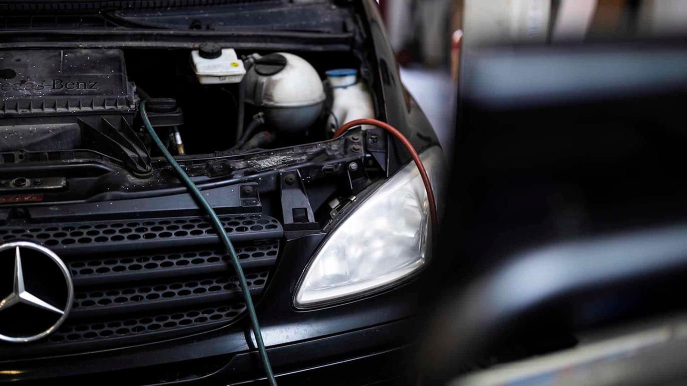 En sort Mercedes bil med åbent motorhjelm, synlig kølevæske og ledninger til batteriopladning.