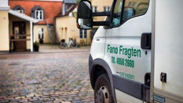 En varevogn fra Fanø Fragten parkeret på en brostensbelagt gade med bygninger i baggrunden.