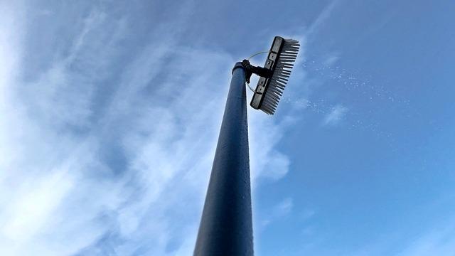 En høj lygtepæl med en børste, der strækker sig mod en blå himmel med skyer.