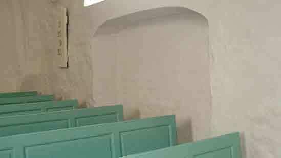Indvendig udsigt af en kirke med grønne bænke og en hvid væg.