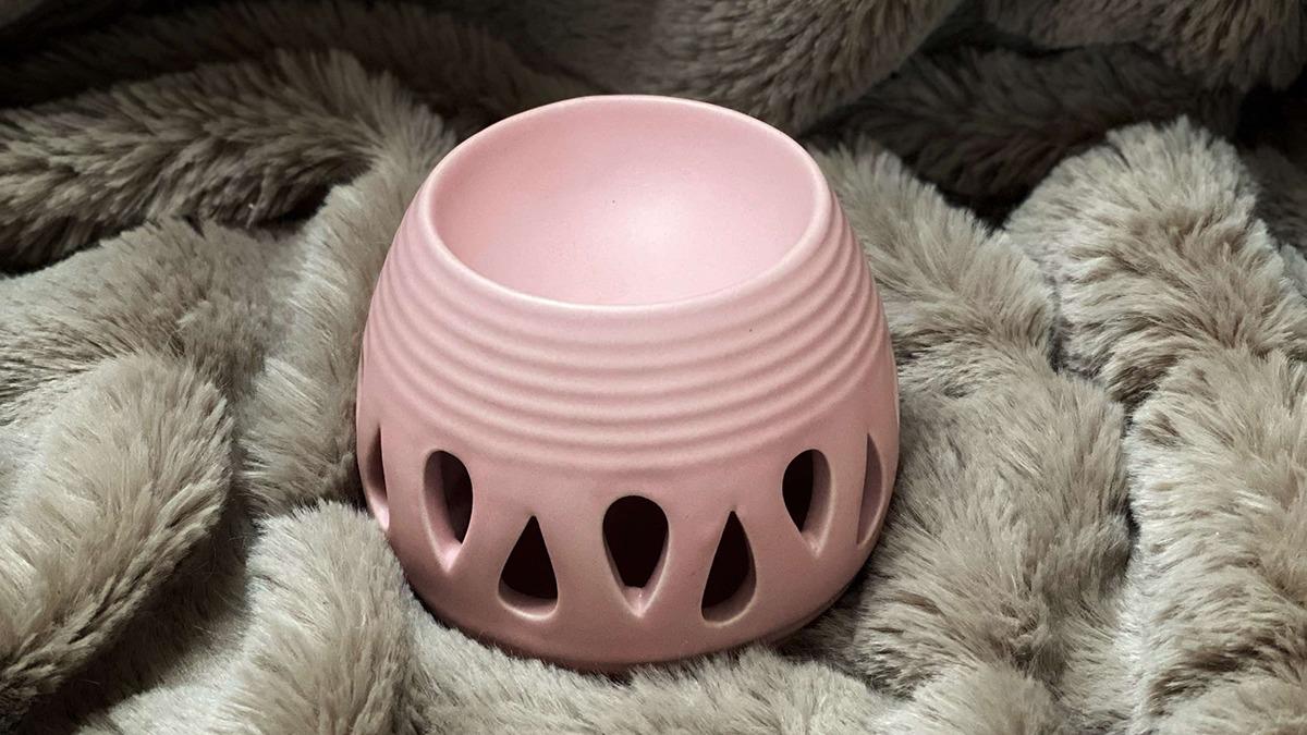 En lyserød skål med dekorative udskæringer, placeret på en blød, grå pels.